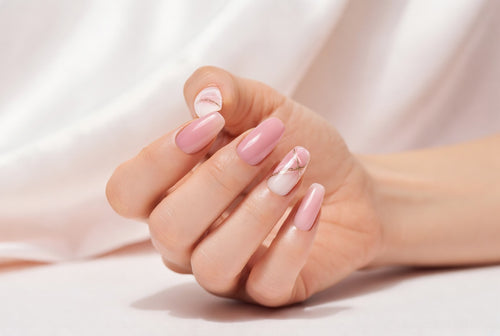 Close-up of a woman's hand showcasing elegant long pink and white marble nails with delicate gold lines on a soft light background